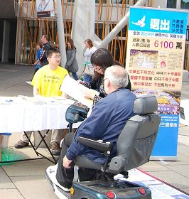 坐电动轮椅车的老先生写字不方便,他请学员帮他把名字写在征签表上