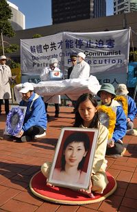 '新西兰法轮功学员在奥克兰市中心举办揭露中共十二年迫害,呼吁制止迫害的活动。图为法轮功小学员开心怀抱妈妈的遗像在活动中。开心的母亲罗织湘女士因为修炼法轮大法被恶警抓捕十二天后遭迫害致死'