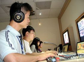 阿亮(前一)在新唐人亚太台负责成音部份。他正为晚间新闻播出的音控工作。