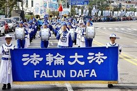 二零一零年十月在韩国仁川的一个市民节日游行中,金先生手持指挥棒引领由法轮功学员组成的军乐队。