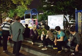 大陆游客逛高雄六合夜市,累了歇一会儿,刚好来看看展板、电视,了解法轮功真相。