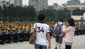 '大陆及来自各地的游客为场中七千多名学员的盛大场面所吸引,有的拿起相机拍照留念。'