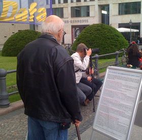 '一位德国老人站在展板前仔细观看,展板上写着中共在历次政治运动中犯下的罪行。'