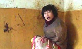 柳志梅常常不穿裤子,只裹一条单薄的床单坐在炕上。身后墙上的黑色黄色是她涂抹大便留下的印迹。(摄于二零一一年冬)