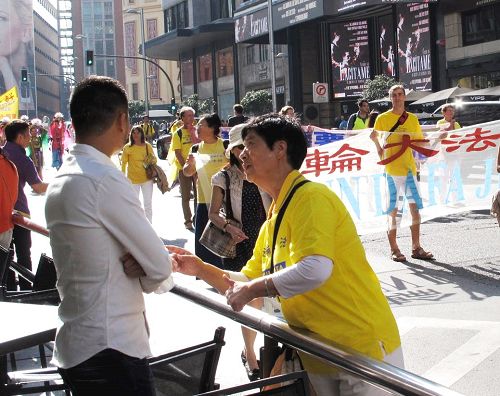 图4:一位亚裔面孔的男青年正在认真观看法轮功大游行,法轮功学员走上前去与他亲切交谈