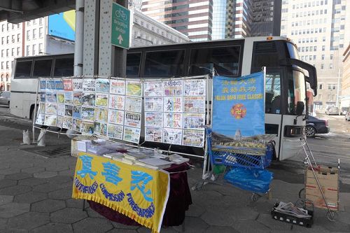'真相展板后面是大陆游客大巴。参观完自由女神像回来的游客在此集合,他们边等人边看真相。右边蓝色小推车,每天将这里的真相条幅、资料收纳整齐。退党义工每天风雨无阻,在此坚守了多年。'