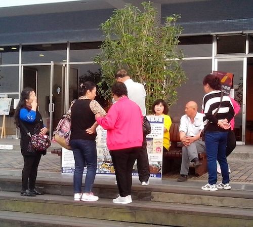大陆游客在休息时观看展板,并与学员(中坐者,穿黄衣服)交谈,了解真相。