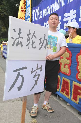 图3:温哥华大陆移民王先生手举“法轮功万岁”的标语牌自发加入集会