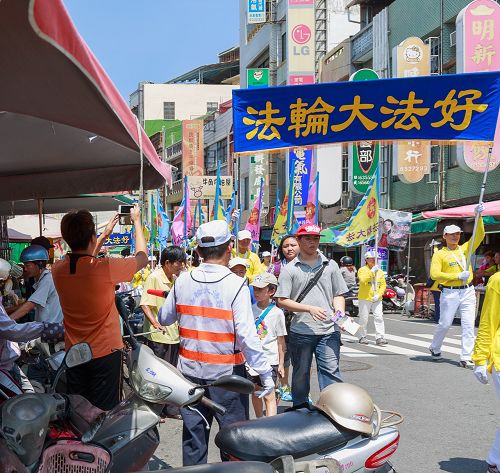 不少民众远远听到法轮功洪法队伍鼓乐声,早已聚集路旁等待队伍的到来,高举着手机、相机拍照留念。