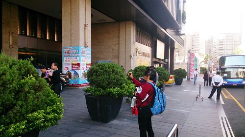 大陆游客在饭店前拍照留念,腋下夹的是学员刚派发给她的真相资料。