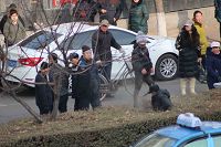 图2:在树丛中蹲坐着的人是崔会芳的亲友,开庭前因给聚集在法院门口的便衣讲真相,而被便衣打骂,被抬着扔到马路中间的绿化带。