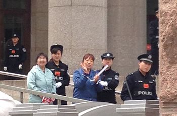 两名法轮功学员被戴了手铐、脚镣,在法院门口她们微笑着向亲人致意