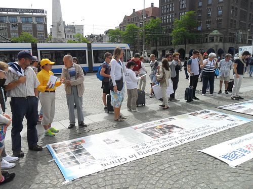 图2-7:荷兰学员在首都阿姆斯特丹达姆广场向各国游客传播真相,他们有的认真阅读真相展板,有的签名支持制止迫害,起诉迫害元凶江泽民。