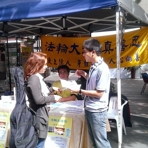图1. 师大学生卓廷威(右一)从小过敏体质,健康不佳,悲观消极,幸于高二开始修炼法轮功,否极泰来,身心和人生观都有意想不到的改善。图为二零一四年十月师范大学校内举办法轮大法周,卓廷威向外籍交换生介绍法轮大法。