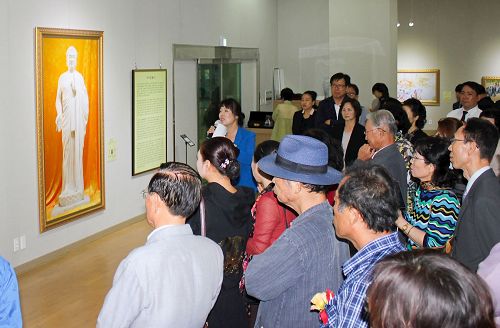 '图2:前来观看美展的各界人士在认真听解说员讲解每幅画的背景。'