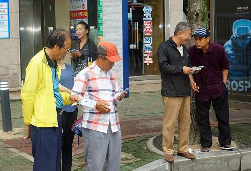 '图4:两旁的民众接过法轮功学员分发的真相资料后,马上阅读。'