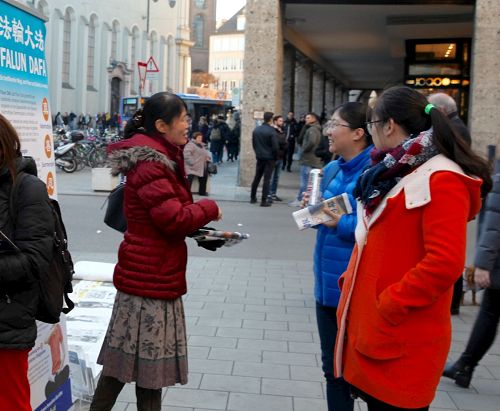 '图6:慕尼黑的法轮功信息展位上,一位法轮功学员(左)正在向两位华人讲述法轮功真相。'