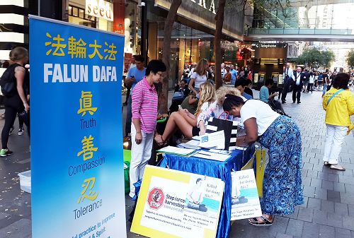 图3:伊溯竹 (Isuzu Dortch)在真相摊位前在给澳洲总理的明信片上签名