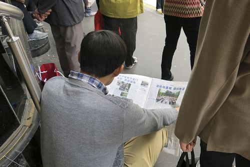 图2:一名大陆游客坐在商场门前的台阶上认真地阅读真相资料,了解法轮功真相。