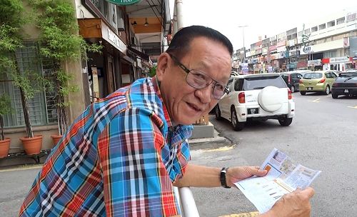 '图17:当地老居民周先生,在法轮功游行队伍走过后,仍然逗留在同样地方细心的阅读法轮功简介。'