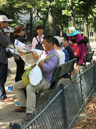 '图4:大陆游客在巴黎埃菲尔铁塔下休息时,认真阅读退党义工发送给他们的《真相报》。'