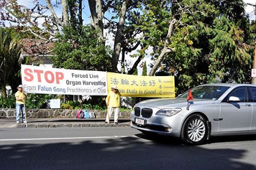 '图2:3月28日下午,李克强一行离开新西兰总督府,经过法轮功学员们的横幅'