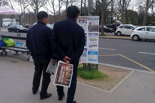 '在巴黎埃菲尔铁塔旁的法轮功真相点上,两名中国大陆游客在接过《法轮功真相报》和大纪元推出的《共产党百年真相》特刊后,认真的观看揭露中共迫害法轮功的真相展板。'