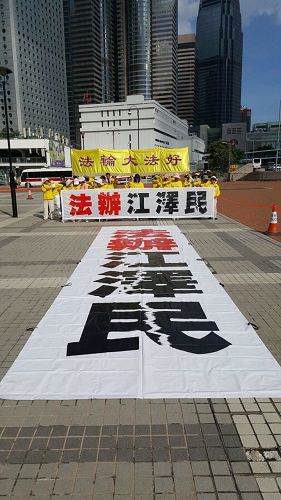'图5~6:香港法轮功学员于三十日早晨,在爱丁堡广场集体炼功,并在正面遥对习近平住宿的海景万丽酒店方向,打出“法办江泽民”的巨型横幅。'
