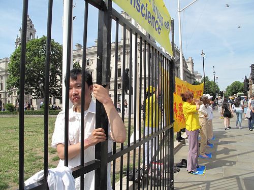 '图5:二零一七年七月十八日,杨博士在英国议会大厦前扮演模拟牢笼中的学员'