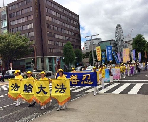 '图1~2:八月五日(星期六),法轮功学员们从早上七点开始在爱知县名古屋市中心的荣公园(Sakae Park)炼五套功法,之后在最繁华地区的荣(Sakae)举办游行。游行队伍由精神抖擞的天国乐团引领,其后是打着“法轮大法好”、“真善忍”、“呼吁停止迫害法轮功”等横幅的队伍。'