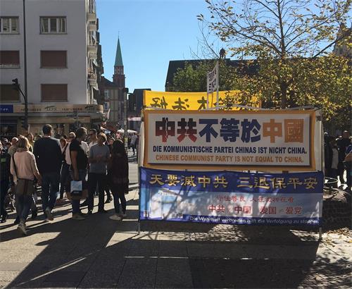 '图4:在市中心的法轮功信息台前,法轮功学员(右二)在给过往行人讲述真相。'
