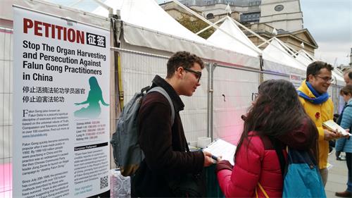 图3:二零一八年十月二十七日,伦敦学生西奥(Theo,左)在特拉法加(Trafalgar Square)广场与法轮功学员一起向路人发真相传单、征签