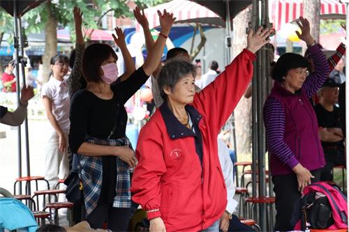 '图4~5:台上法轮功学员功法演示,台下游客也跟着做动作一起学炼。'