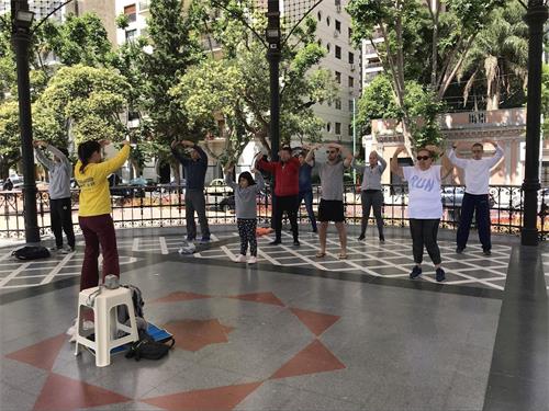 '在市区内的炼功点,小女孩和妈妈经过时,看到法轮功学员祥和的炼功场面,也加入其中。'