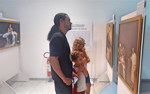 '图2:这位职员带孩子观看“真善忍美展”,并给孩子们读画作的解说词。他说,观画作,如打对中共的预防针。'