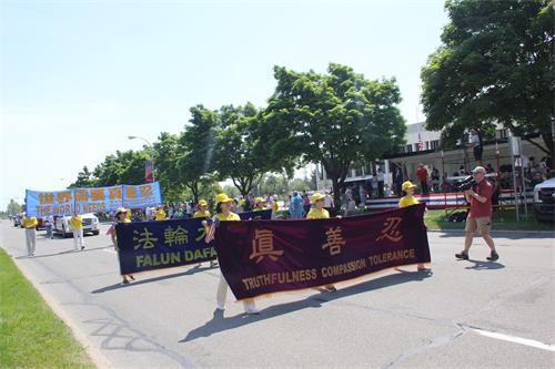 '图4:密西根州法轮大法学会的方阵走过主席台,迪尔本市电台在摄像'