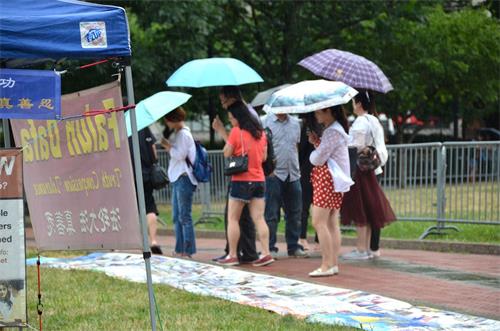 '图7:集会期间下起了大雨,但中国大陆游客仍冒雨观看揭露中共迫害法轮功的真相展板。'