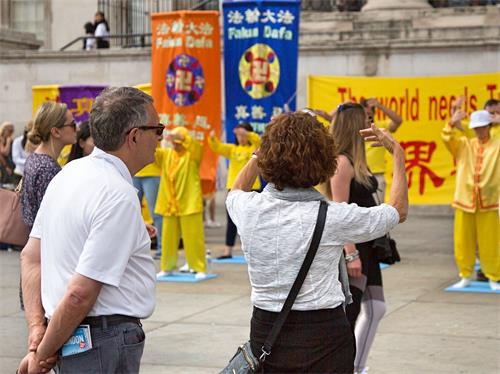 '图6~7:人们被祥和的能量场吸引,有的跟学员交谈了解真相,有的模仿学员的炼功动作 。'