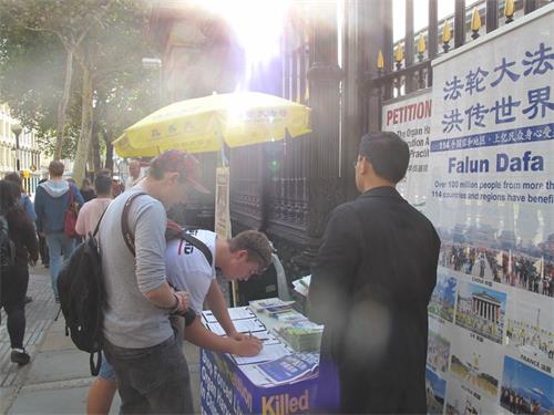 '图12:二零一八年八月二十五日傍晚,在大英博物馆南门入口,两个伦敦男学生观看法轮功学员炼功打坐和真相展板后立即签名要求“停止活摘法轮功学员器官停止迫害法轮功”'