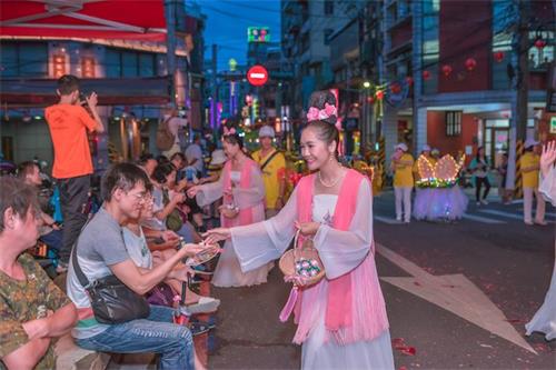 '图3:青年法轮功学员装扮的仙女队向两旁观众发放莲花'
