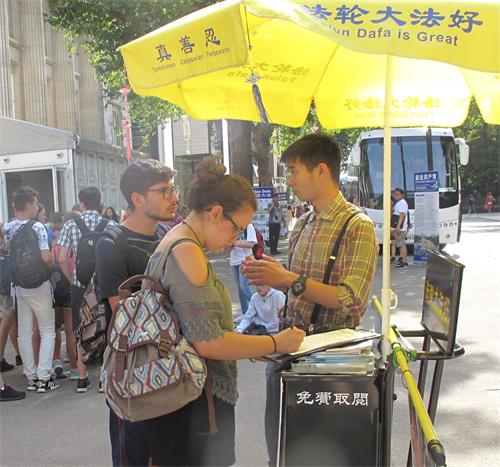 '图2:一对青年游客驻足认真了解真相后签名支持法轮功反迫害'