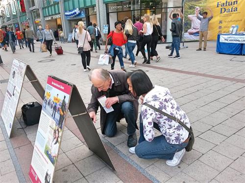 '图5:两位路人蹲下阅读真相展板。'