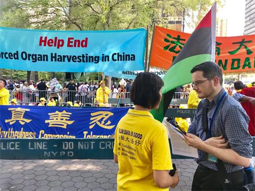 '图1:福克斯新闻记者亚当·萧(Adam Shaw,右)站在“请帮助结束发生在中国的大屠杀”(Help End Genocide in China)条幅前,采访法轮功学员简(Jane)。'