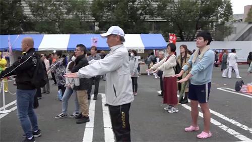 '图3~4:学员在舞台上表演功法时,许多台下的观众跟着模仿学员的炼功动作。'