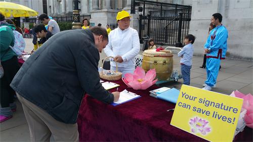 图4~5:在伦敦特拉法加广场北台阶,民众为“世界法轮大法日”庆祝活动所吸引,驻足了解真相,他们在明白真相后纷纷签名支持法轮功反迫害。