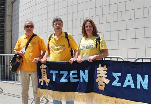 '图29:斯塔斯(Kostas,中)与来自希腊的同修拿着希腊文“真、善、忍” 横幅,在游行起点等候,整装待发。'