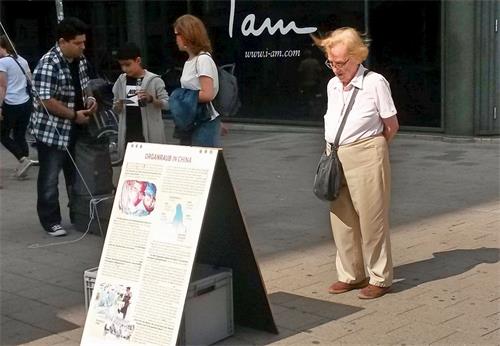 '图11:这位女士仔细阅读了关于中国法轮大法学员被强摘器官的信息展板,感到十分震惊。'