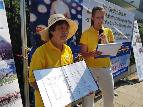 '图3:在集会中,许女士向民众展示酷刑示意图,法轮功学员用许女士的亲身经历作为例子,讲述了中共对法轮功学员的酷刑迫害。'