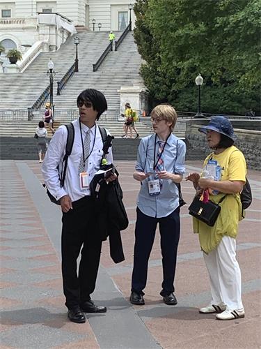 图16:两位年轻人一边看着旁边的集会横幅,一边听法轮功学员讲述真相