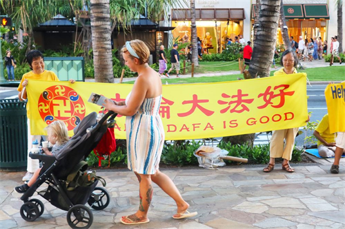 '图5:一位西方年轻妈妈路过法轮大法横幅前边走边看手里的真相传单'